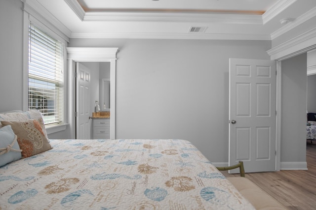 bedroom featuring a raised ceiling, crown molding, hardwood / wood-style floors, and ensuite bathroom