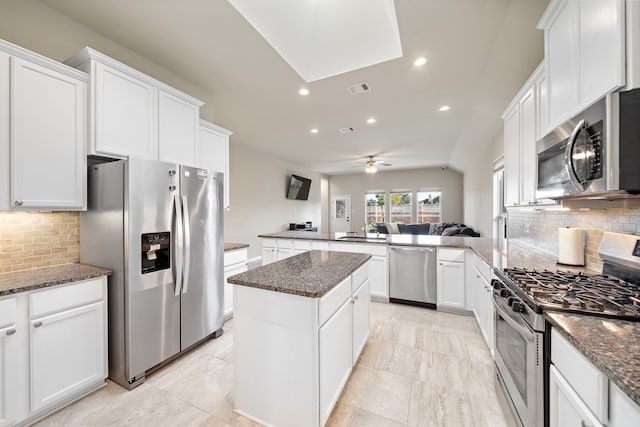 kitchen featuring appliances with stainless steel finishes, a center island, ceiling fan, and dark stone countertops