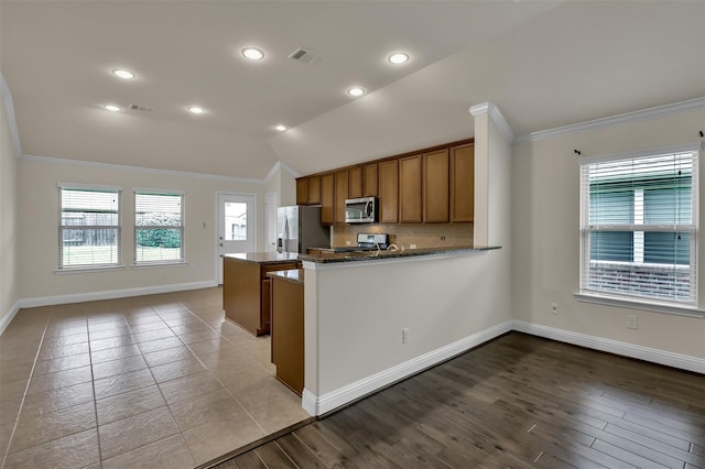 kitchen with stainless steel appliances, kitchen peninsula, dark stone counters, lofted ceiling, and light wood-type flooring