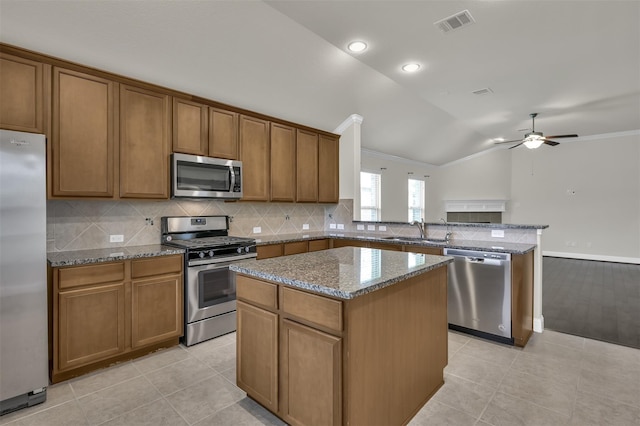 kitchen featuring lofted ceiling, sink, light stone countertops, a kitchen island, and stainless steel appliances