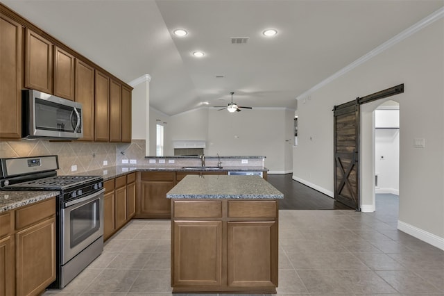 kitchen featuring stainless steel appliances, vaulted ceiling, sink, a barn door, and a center island