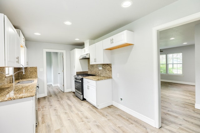 kitchen with backsplash, white cabinets, stainless steel range with gas cooktop, sink, and light stone countertops