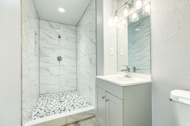 bathroom with a tile shower, vanity, and toilet