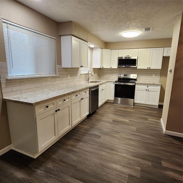 kitchen featuring appliances with stainless steel finishes, a textured ceiling, light stone counters, white cabinets, and sink