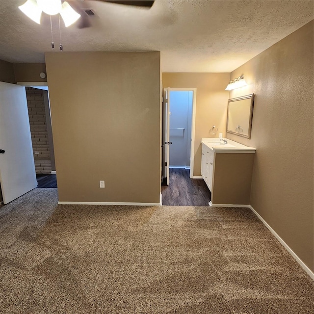 interior space featuring a textured ceiling, dark colored carpet, ceiling fan, and sink