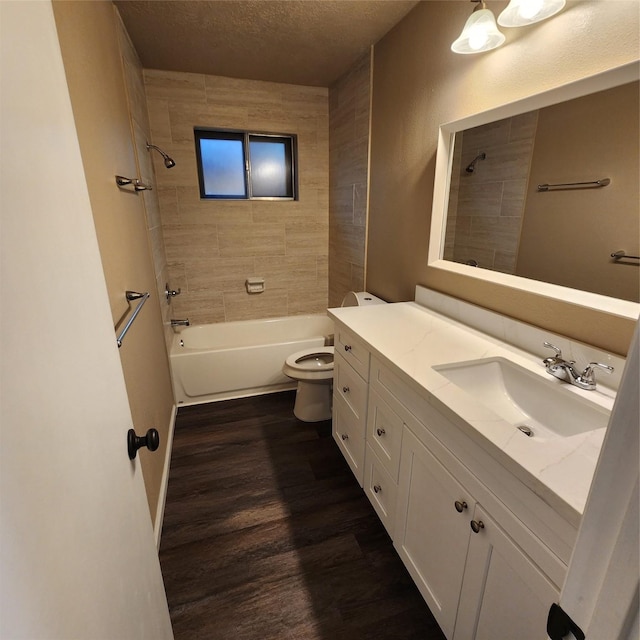 full bathroom featuring a textured ceiling, tiled shower / bath, hardwood / wood-style floors, toilet, and vanity