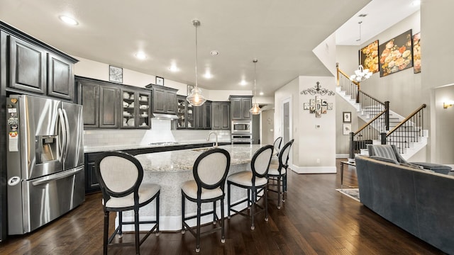 kitchen featuring a kitchen island with sink, hanging light fixtures, stainless steel appliances, light stone countertops, and decorative backsplash