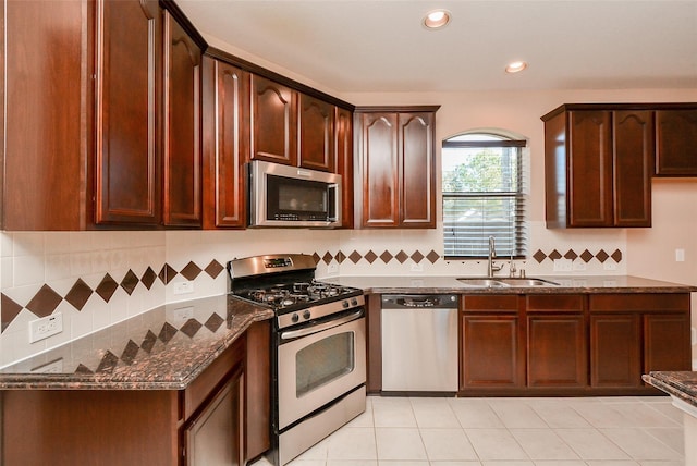 kitchen with light tile patterned flooring, stainless steel appliances, dark stone countertops, and sink