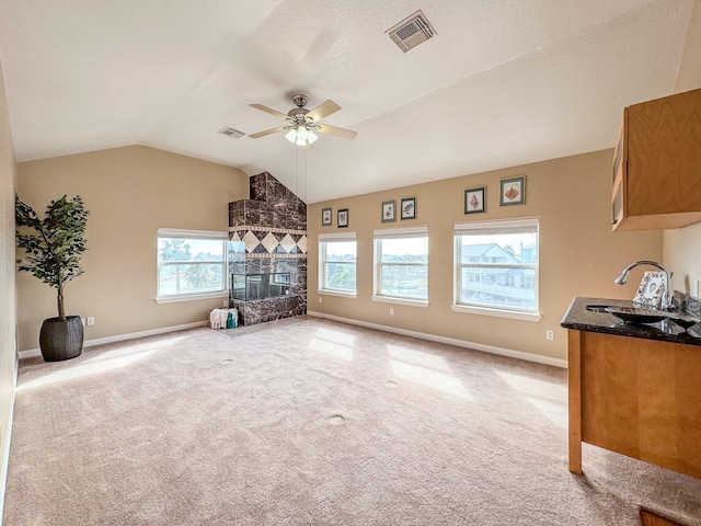 unfurnished living room with ceiling fan, sink, vaulted ceiling, light carpet, and a fireplace