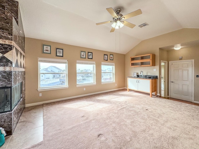 unfurnished living room with ceiling fan, light colored carpet, lofted ceiling, and a fireplace