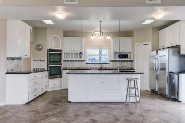 kitchen with white cabinetry, an island with sink, decorative light fixtures, a kitchen bar, and appliances with stainless steel finishes