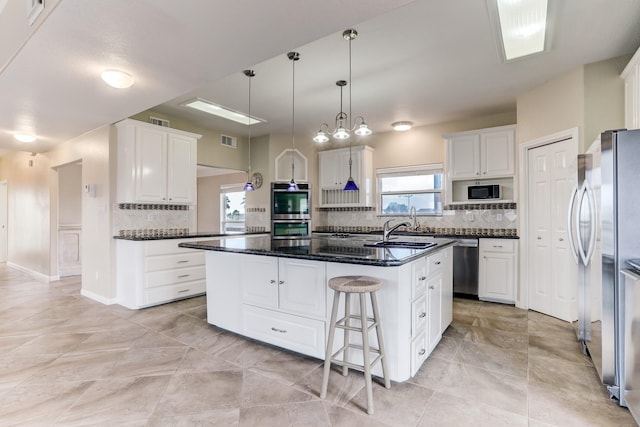 kitchen with white cabinets, appliances with stainless steel finishes, a kitchen bar, and an island with sink