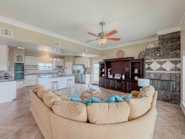 tiled living room with ceiling fan, ornamental molding, and a fireplace