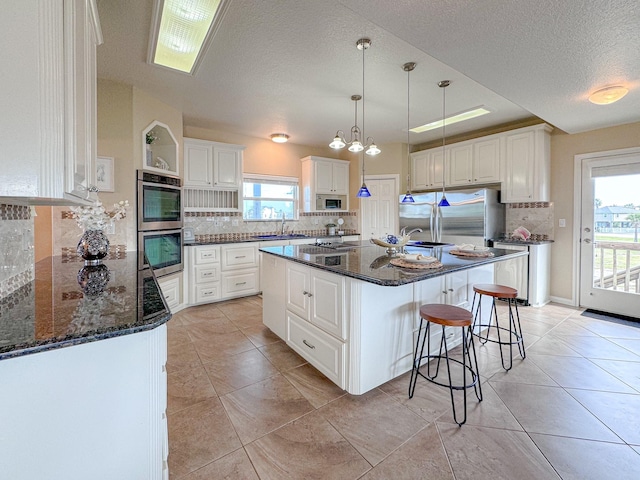 kitchen with appliances with stainless steel finishes, a healthy amount of sunlight, sink, white cabinets, and a center island