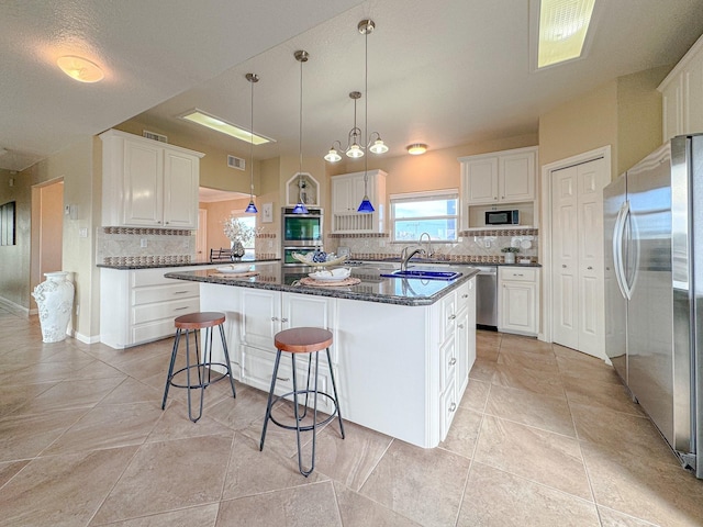 kitchen with appliances with stainless steel finishes, tasteful backsplash, a kitchen island with sink, sink, and white cabinetry