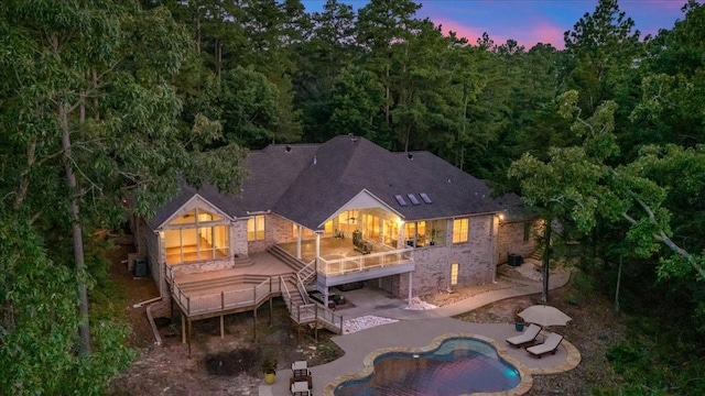 back house at dusk featuring a swimming pool side deck and a patio