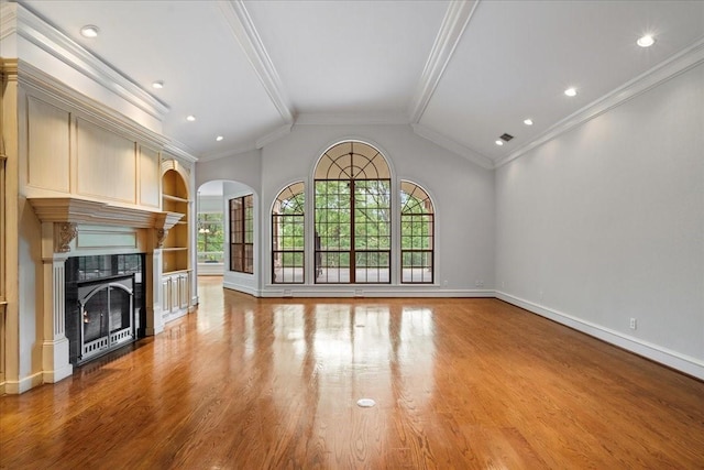 unfurnished living room with built in shelves, crown molding, a tiled fireplace, and light wood-type flooring