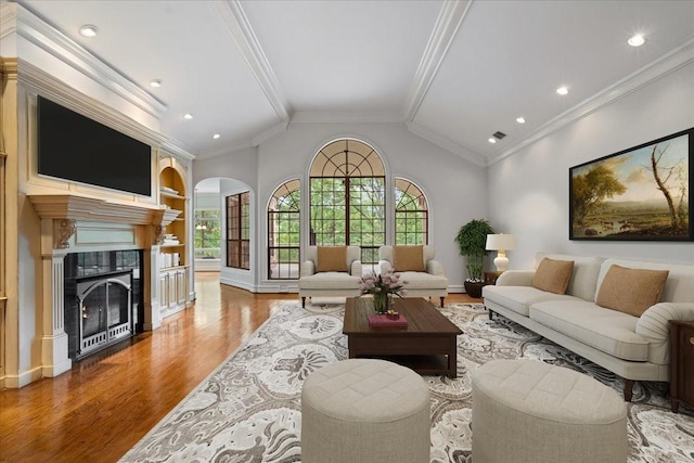 living room with built in shelves, crown molding, light hardwood / wood-style flooring, a fireplace, and lofted ceiling