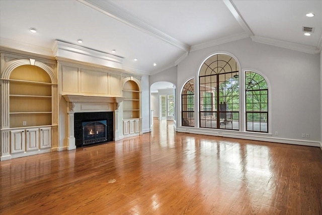 unfurnished living room with built in shelves, crown molding, a fireplace, and hardwood / wood-style flooring