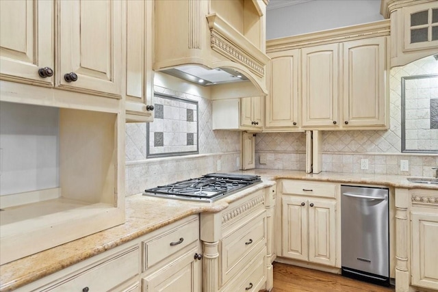 kitchen featuring light wood-type flooring, tasteful backsplash, custom exhaust hood, stainless steel appliances, and cream cabinetry