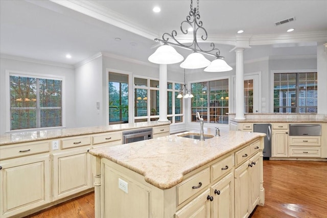 kitchen with light stone counters, ornamental molding, pendant lighting, a center island with sink, and cream cabinetry