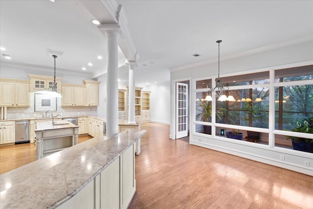 kitchen featuring crown molding, light stone countertops, ornate columns, cream cabinetry, and a notable chandelier