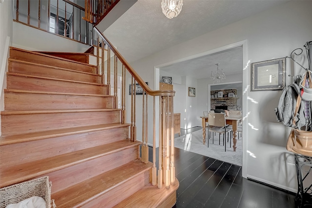 stairway featuring wood-type flooring, a notable chandelier, and a brick fireplace