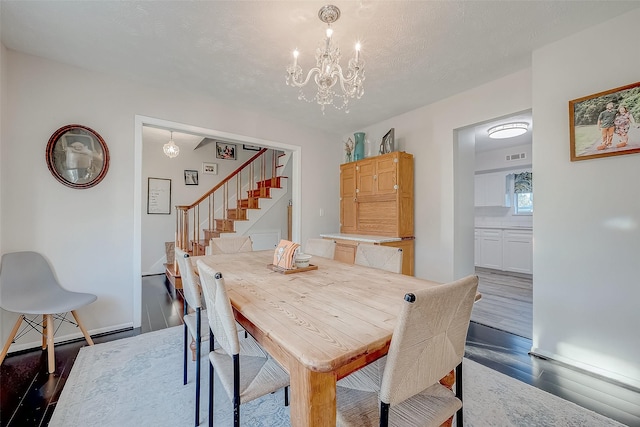 dining space featuring dark wood-type flooring, a textured ceiling, and a notable chandelier