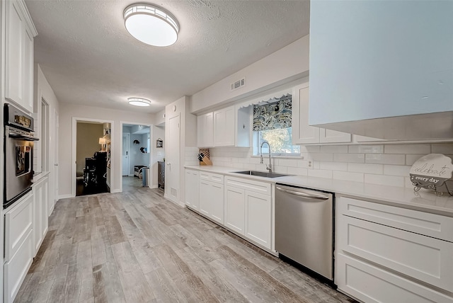 kitchen featuring sink, tasteful backsplash, light hardwood / wood-style floors, white cabinets, and appliances with stainless steel finishes