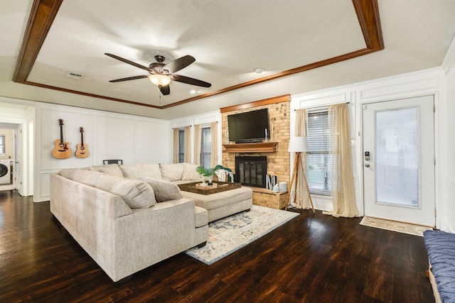 living room featuring ornamental molding, washer / clothes dryer, ceiling fan, a fireplace, and dark hardwood / wood-style floors