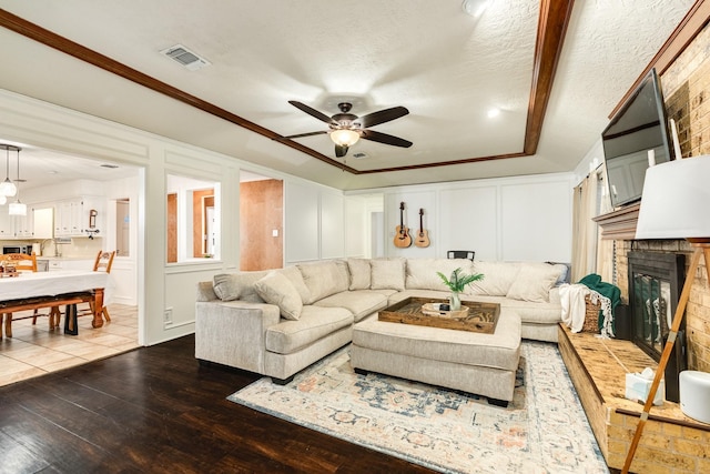 living room featuring ornamental molding, a textured ceiling, ceiling fan, wood-type flooring, and a fireplace