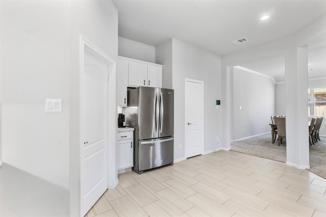 kitchen featuring light carpet, stainless steel fridge, white cabinetry, and ornamental molding