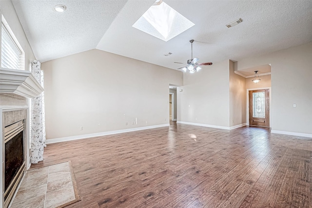 unfurnished living room featuring a textured ceiling, a wealth of natural light, hardwood / wood-style flooring, lofted ceiling with skylight, and a tiled fireplace