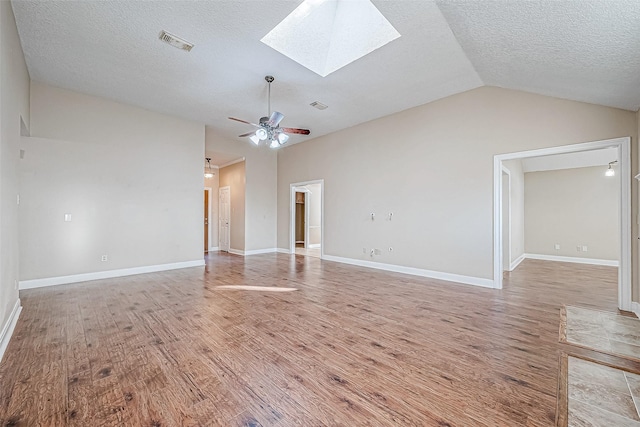 unfurnished living room with ceiling fan, vaulted ceiling with skylight, a textured ceiling, and light wood-type flooring