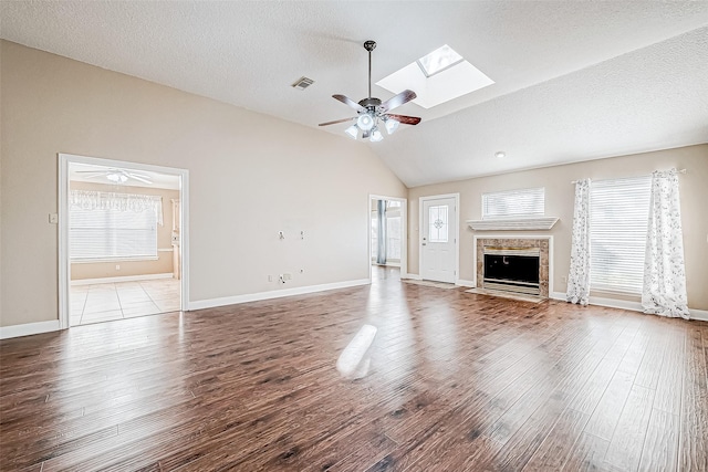 unfurnished living room featuring ceiling fan, vaulted ceiling with skylight, light hardwood / wood-style floors, and plenty of natural light