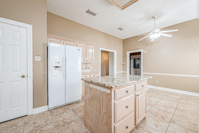 kitchen featuring ceiling fan, a kitchen island, light stone countertops, a textured ceiling, and white fridge with ice dispenser