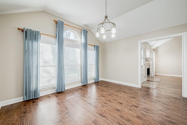 unfurnished dining area featuring vaulted ceiling, a notable chandelier, a textured ceiling, and hardwood / wood-style flooring