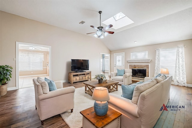 living room with ceiling fan, a tile fireplace, wood-type flooring, and lofted ceiling with skylight