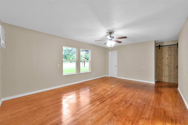 empty room featuring ceiling fan, a barn door, a textured ceiling, and light hardwood / wood-style flooring