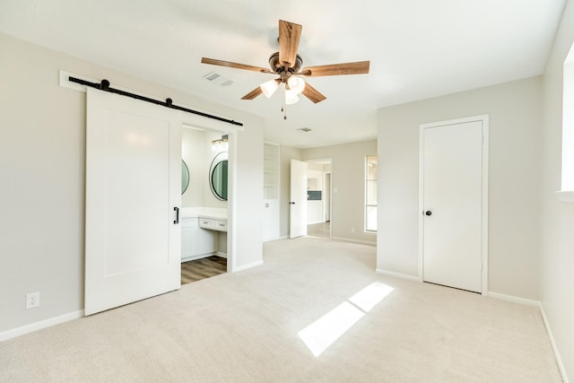 unfurnished bedroom with ceiling fan, connected bathroom, light carpet, and a barn door