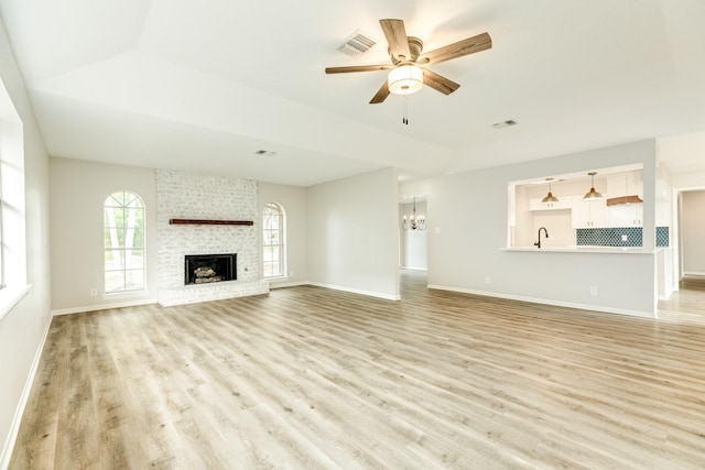 unfurnished living room featuring ceiling fan with notable chandelier, plenty of natural light, light hardwood / wood-style flooring, and a fireplace