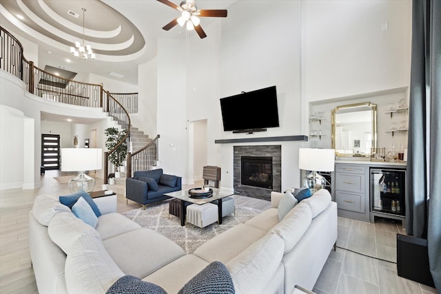 living room with a tray ceiling, a tile fireplace, bar area, a high ceiling, and wine cooler