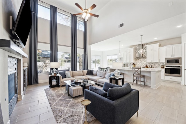 tiled living room featuring ceiling fan, a high ceiling, and a brick fireplace