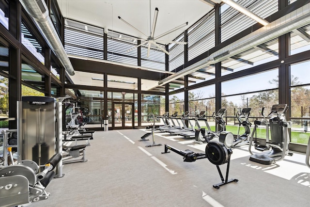 exercise room featuring carpet, ceiling fan, plenty of natural light, and a high ceiling