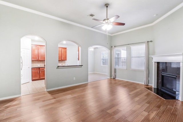 unfurnished living room with a tile fireplace, light wood-type flooring, ceiling fan, and ornamental molding