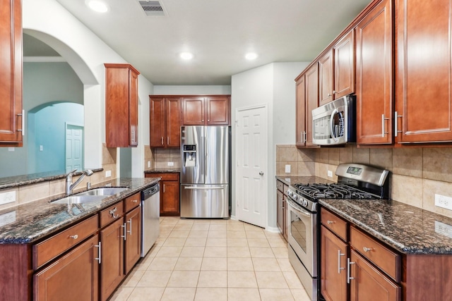 kitchen with dark stone countertops, light tile patterned flooring, sink, and stainless steel appliances