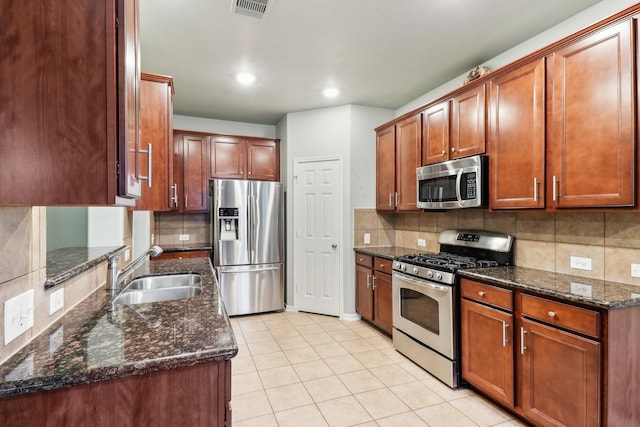 kitchen with sink, backsplash, dark stone counters, light tile patterned flooring, and appliances with stainless steel finishes