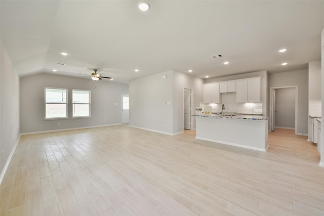 unfurnished living room with ceiling fan, sink, vaulted ceiling, and light wood-type flooring