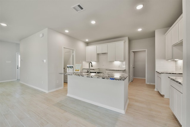 kitchen featuring decorative backsplash, sink, stone countertops, white cabinets, and an island with sink