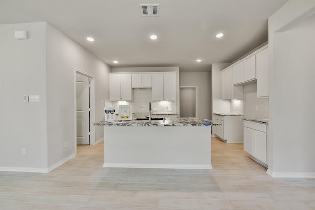 kitchen with white cabinetry, an island with sink, and light stone countertops